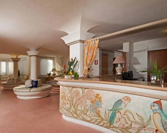 Reception con bancone decorato con pappagalli e fiori, interni eleganti e luminosi.