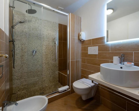 Moderno bagno con doccia, lavabo tondo e piastrelle marroni.