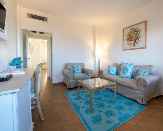 Soggiorno con divano, poltrona, tappeto azzurro, tavolino e lampada.