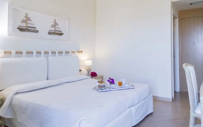 Camera d'albergo con letto matrimoniale, quadro di barche a vela e colazione su vassoio.