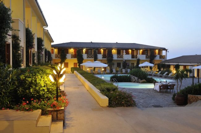 Edificio giallo, piscina illuminata, ombrelloni e lettini in un cortile all'aperto.