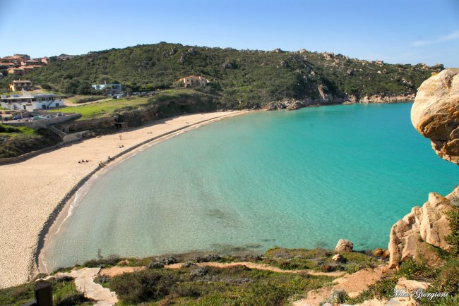 Spiaggia sabbiosa con mare turchese, circondata da colline verdi.
