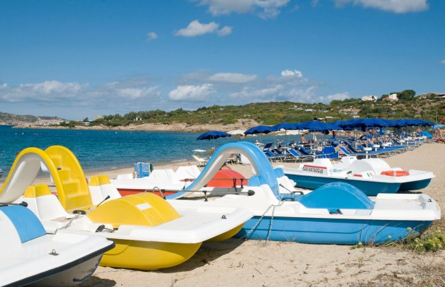 Pedalò colorati sulla spiaggia con ombrelloni blu e mare sullo sfondo.