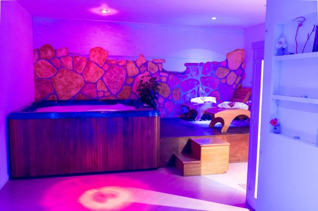 Una stanza con Jacuzzi e lettino relax, illuminata da luci colorate.