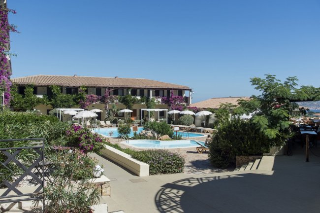 Piscina esterna circondata da ombrelloni e vegetazione, cielo azzurro.