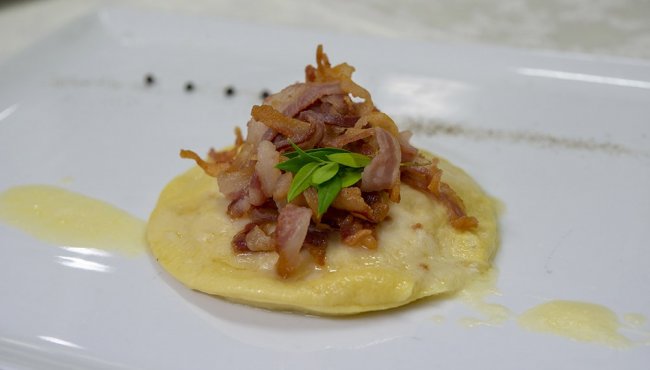 Piatto di raviolo con pancetta croccante e foglia verde sopra.