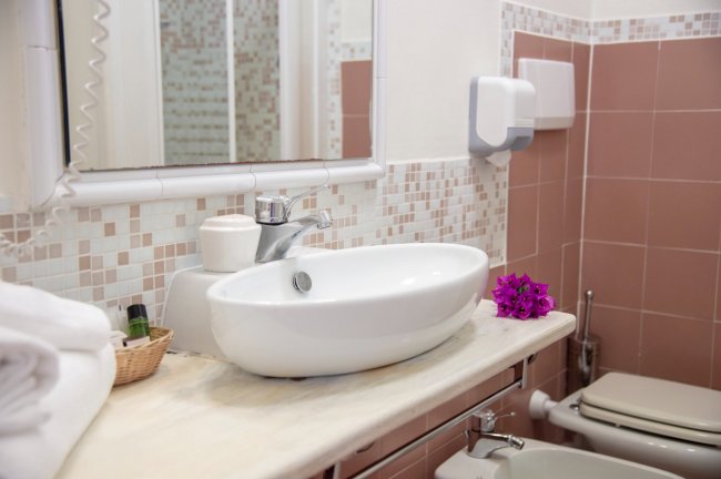 Bagno con lavabo ovale, asciugamani e piastrelle rosa.