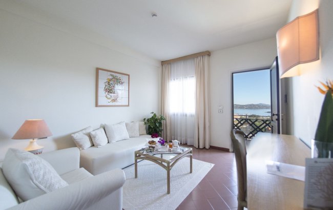 Soggiorno luminoso con divano bianco, tavolino da caffè e porta-finestra con vista sul mare.