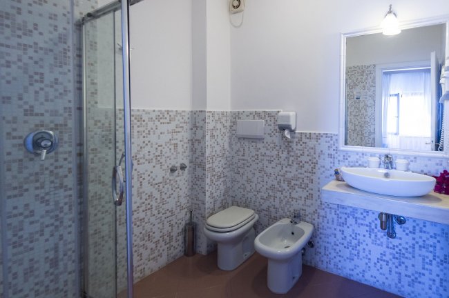 Bagno moderno con box doccia trasparente, wc, bidet e lavabo su piano in pietra chiara.