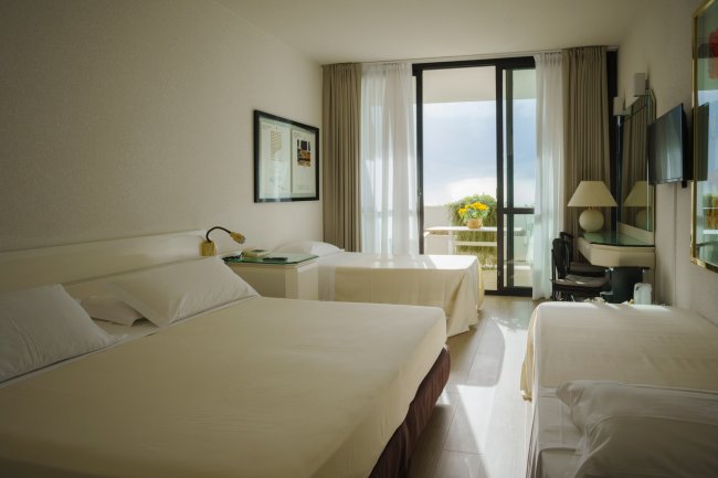 Camera d'hotel con tre letti e balcone.