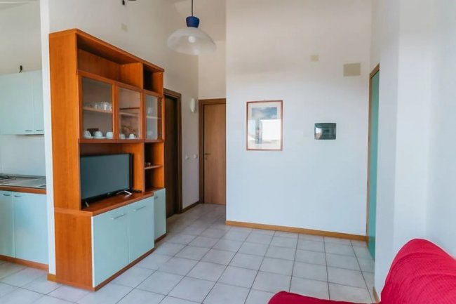 Sala luminosa con armadio TV e cucina vista.