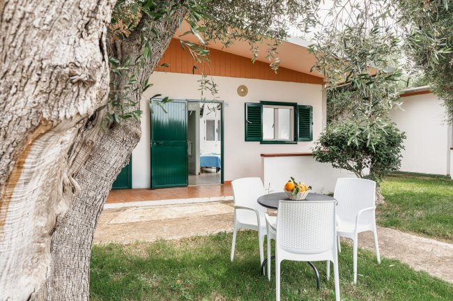 Tavolo bianco con sedie davanti a una casa immersa nel verde.