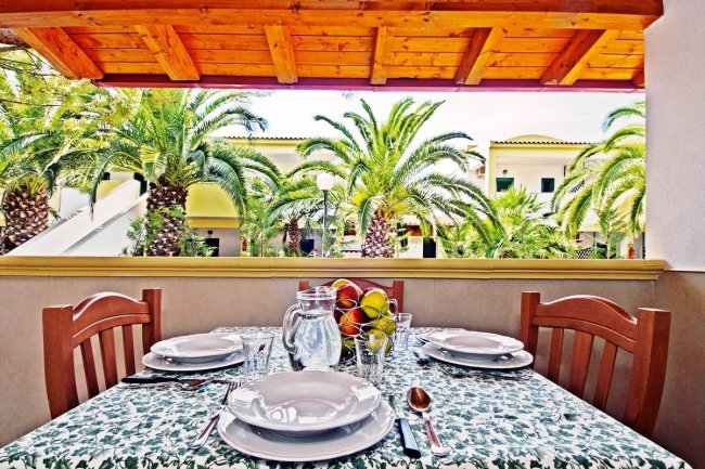 Tavola apparecchiata su terrazza con vista su palme.