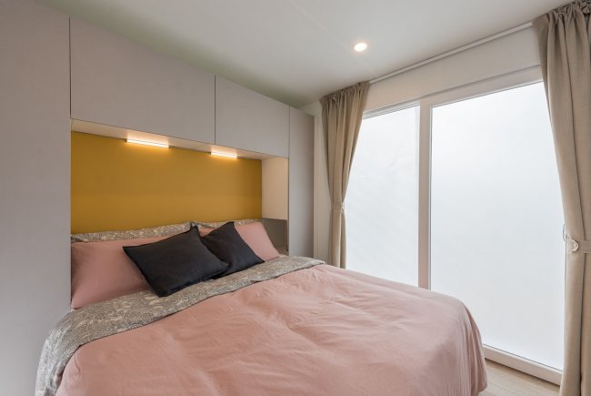 Camera con letto matrimoniale, pareti chiare e tende beige.