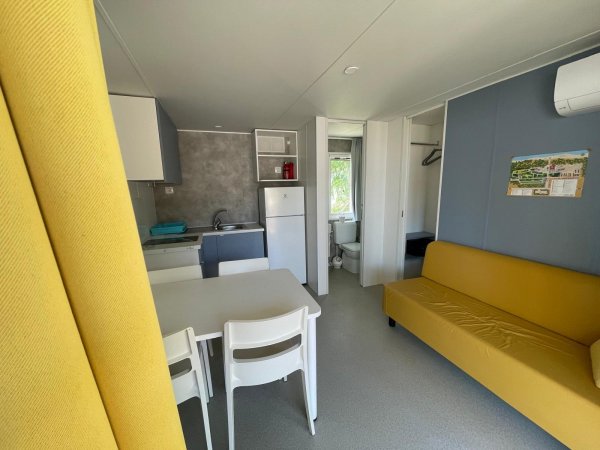 Cucina e soggiorno con divano giallo e sedie bianche.