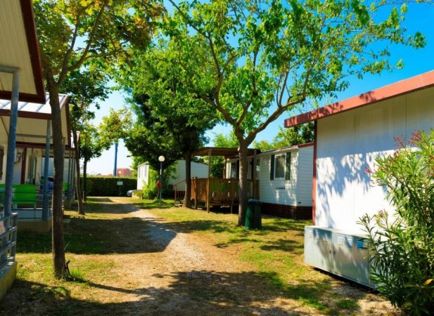 Strada tra case mobili con alberi e prati.