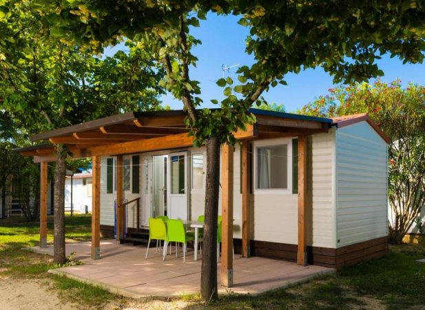 Bungalow con portico e sedie verdi tra gli alberi.