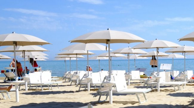 Spiaggia con ombrelloni bianchi e sedie a sdraio.