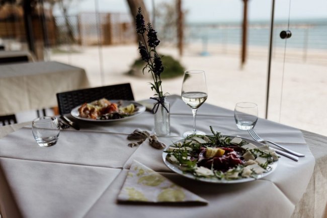 Tavolo apparecchiato all'aperto con piatti e bicchieri di vino.